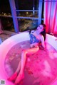 A woman sitting in a bathtub filled with pink liquid.