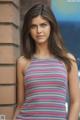 A woman leaning against a brick wall in a striped dress.