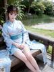 A woman in a blue kimono sitting on a wooden bench.