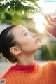 A young girl in an orange sweater looking up at the sky.