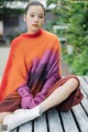 A woman sitting on a wooden bench wearing a colorful sweater.