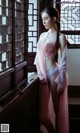 A woman in a pink robe standing by a window.