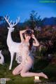 A woman in lingerie sitting on the grass next to a white deer.