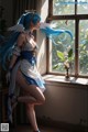 A woman with long blue hair standing in front of a window.