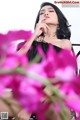 A woman in a black dress sitting on a chair surrounded by pink flowers.