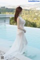 A woman in a white dress standing next to a swimming pool.