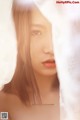 A woman with long brown hair is peeking out from behind a curtain.