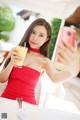 A woman in a red dress taking a selfie with a glass of orange juice.