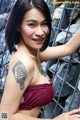 A woman with a tattoo on her arm leaning against a fence.