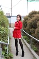 A woman in a red coat is standing on a sidewalk.