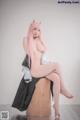 A woman with pink hair sitting on a wooden stool.