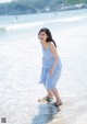 A woman in a blue and white striped dress walking on the beach.